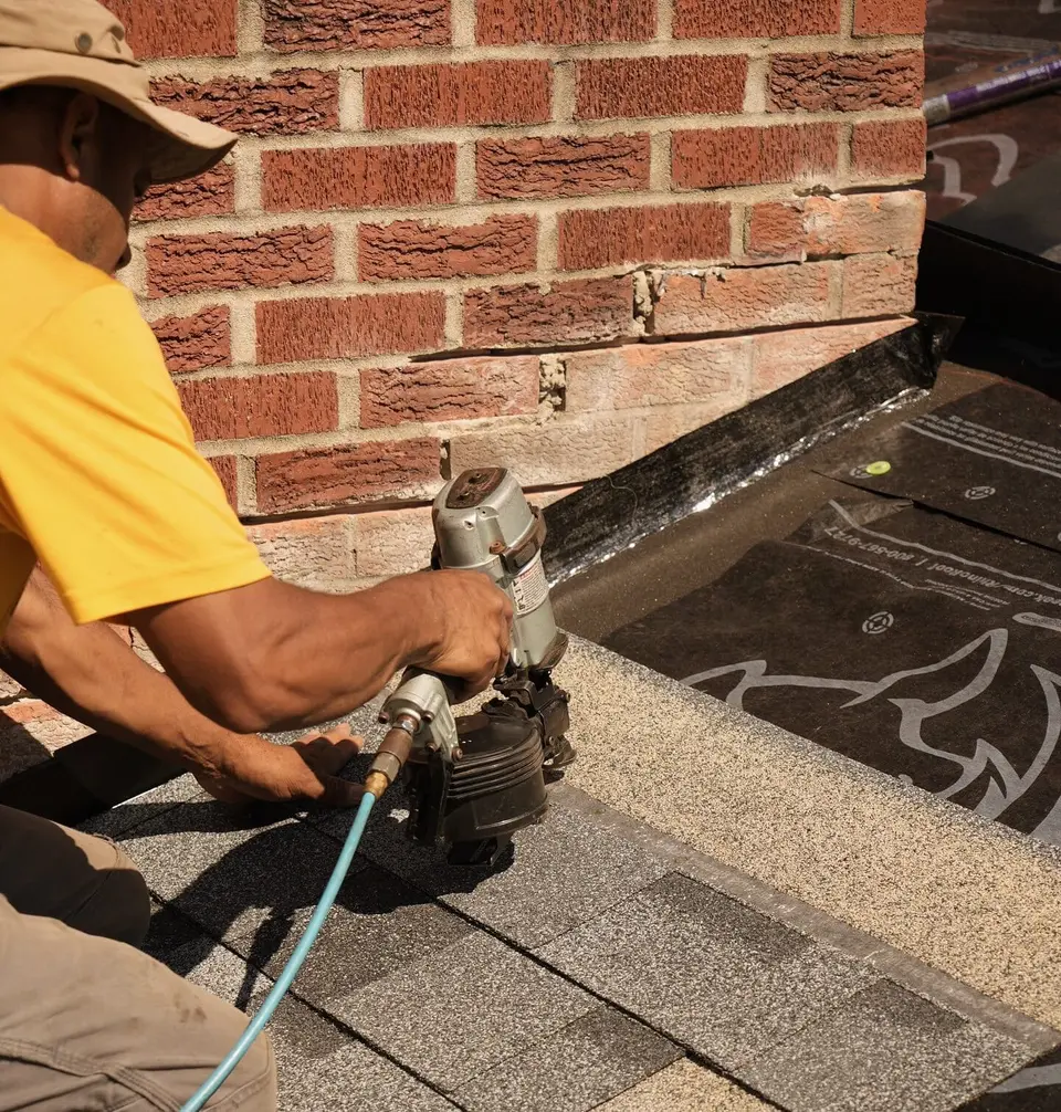Crew member nailing shingles and flashing around a brick chimney
