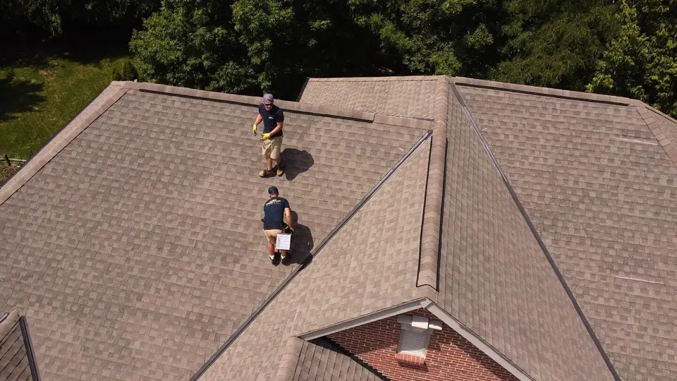 Drone view of two inspectors walking a shingle roof to document hail damage