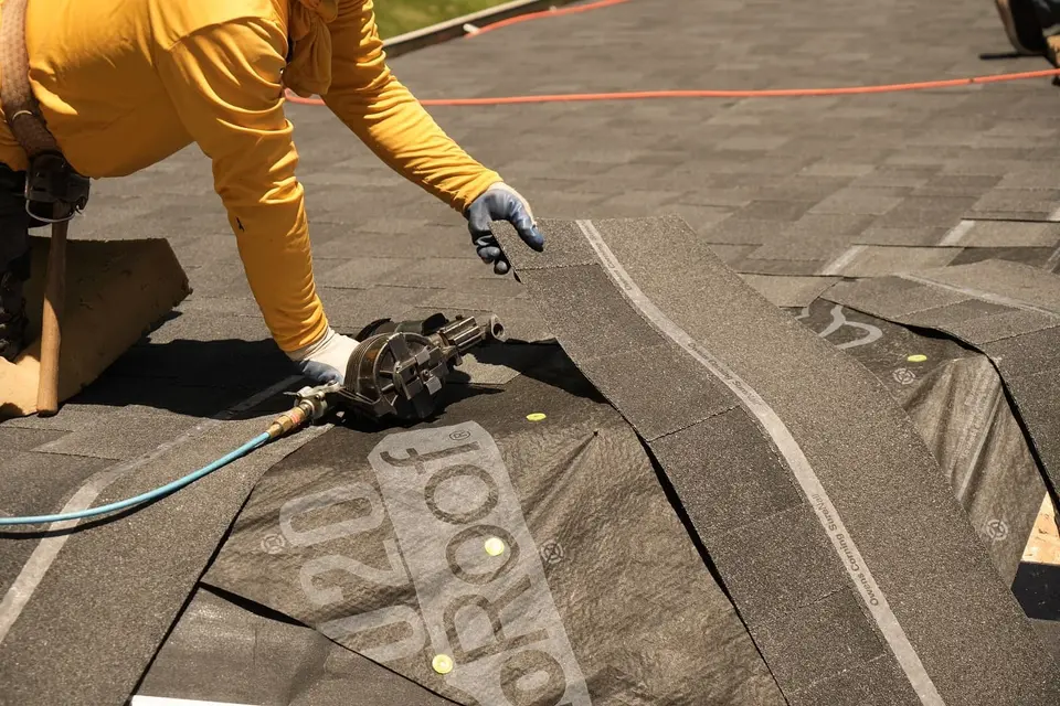 Crew member in a yellow shirt fastening new shingles with a nail gun