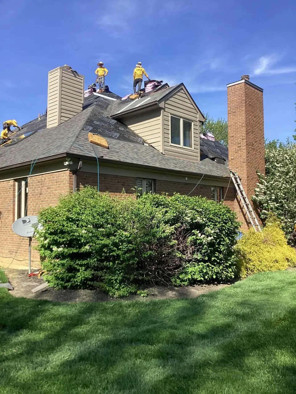 Crew working on a roof replacement with a ladder against a brick chimney